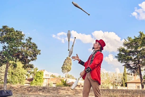 Low angle of male juggler tossing clubs in air while standing on stairs during performance in park on sunny summer day