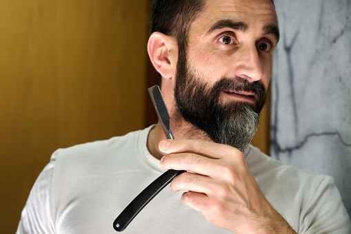 Young man with a beard shaving with a traditional knife in front of the mirror. High quality photo