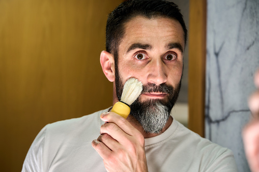 Young man soaping his face with a brush to shave his beard