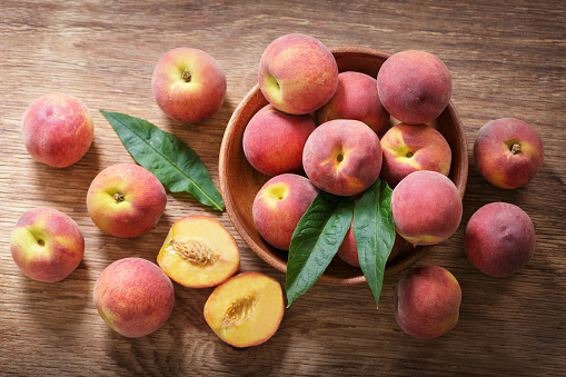 Fresh peaches in a bowl on a wooden table, top view