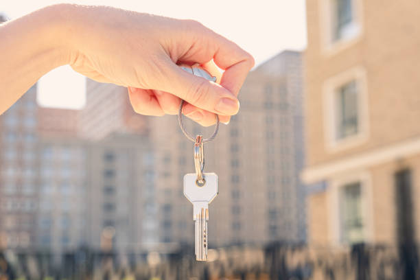 Womans hand holds a key against the backdrop of a multi-storey residential area Woman's hand holds a key against the backdrop of a multi-storey residential area. The concept of buying residential real estate, winning the lottery, affordable mortgage bail law stock pictures, royalty-free photos & images
