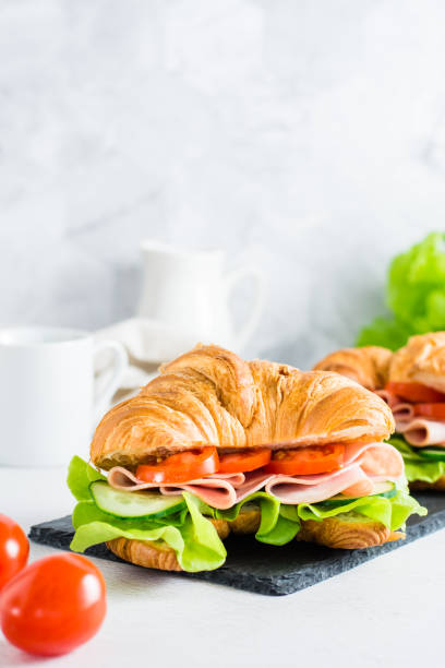 istock Two croissant sandwiches with ham, cucumbers, tomato and lettuce on a slate. Vertical view 1406577753