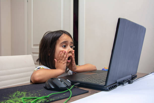 little girl is shocked by what she sees on the computer screen - surprise child little girls shock imagens e fotografias de stock