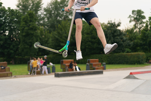 Moscow, Russia - July 13, 2020: Trick in the city skate  park. Push scooter. He jumping over an obstacles. Extreme sports is very popular among youth. Frontal view.