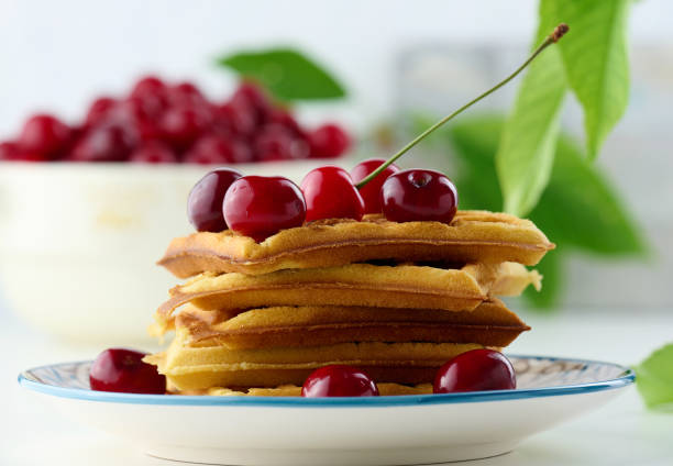 Stack of baked Belgian waffles with ripe red cherries on the white table, breakfast