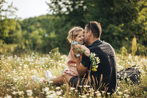 Father with his little daughter having fun together on a meadow in nature. Father is kissing his daughter.