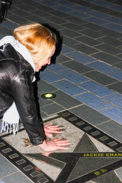 lächelnder heller europäischer blonder mädchenfan, der auf den knien auf der berühmten promenade in kowloon sitzt und seine hände an jackie chans handflächenabdrücke auf der tsim sha tsui promenade legt celebrity avenue stars, hongkong - auszeichnung als bester schauspieler stock-fotos und bilder