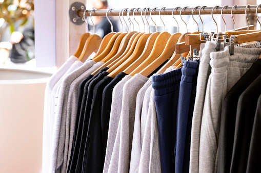 Row of knitted hoodies and pants, sports sweaters hanging on a hangers in Retail store, closeup, background with copy space, full frame horizontal composition