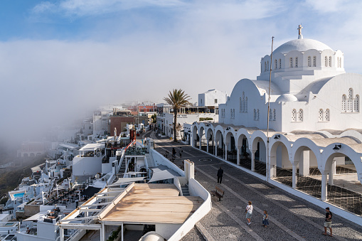 View of Fira and the Orthodox Metropolitan Cathedral, among scenic low clouds in early morning. Fira, Santorini, Greece, Apr. 2022