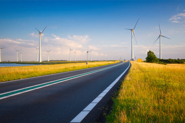 Landscape during sunset with road, field and wind turbines. Windmills for energy production. Green energy in the Netherlands. A beautiful asphalt road with wind power turbines during sunset. stock photo