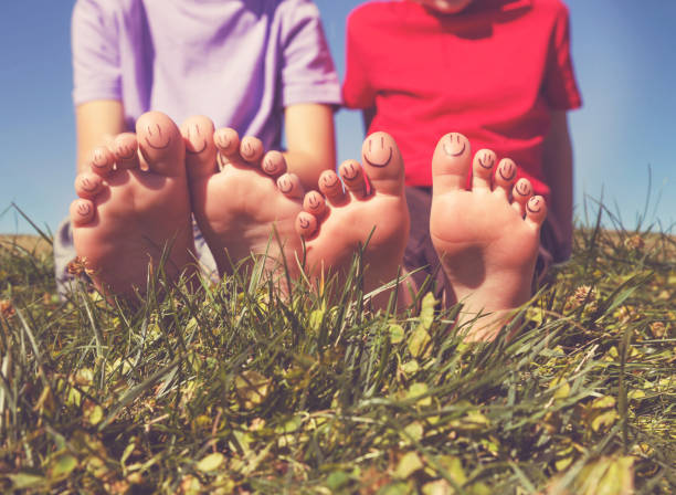 dos niños con caras sonrientes en los dedos de los pies sentados en la hierba tonificada con un filtro retro vintage de instagram - barefoot behavior toned image close up fotografías e imágenes de stock