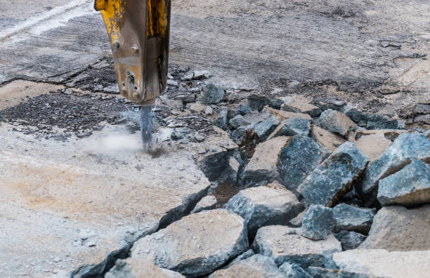 Close-up of demolition hammer with dust and sparks and broken concrete pieces Detail of hydraulic jackhammer mounted on excavator arm working at old road reconstruction. Repairs in civil engineering demolishing stock pictures, royalty-free photos & images