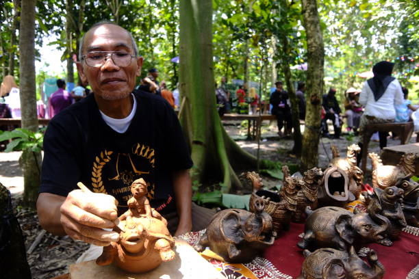 un anciano que es artesano de cerámica talla la forma de warak ngendog en un cenicero que luego se venderá en el mercado de arte indonesio de semarang - parade music music festival town fotografías e imágenes de stock