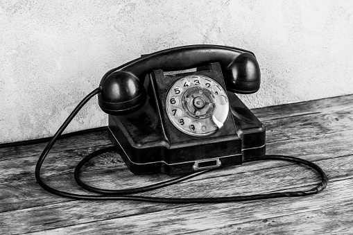 Retro black rotary telephone on wooden table in front gray concrete background