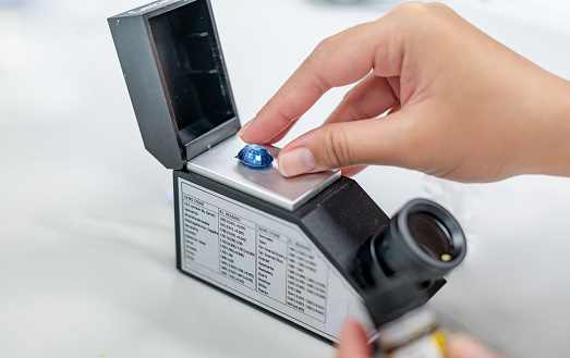 Female hand holding the blue precious stone and put on the refractometer for confirm the type of stone