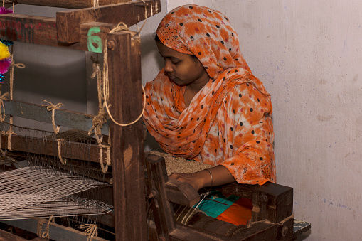 6th April, 2022, Dhupjhora, West Bengal, India: A village woman making hancrafted jute door mat useing jute rope in a hand made machine
