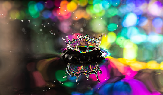 A macro low angle close up of a water drop making a splash in colorful water.