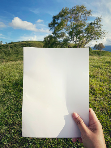 Holding blank paper with nature background.