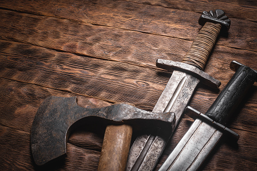 Old battle sword and axe on the wooden table background.