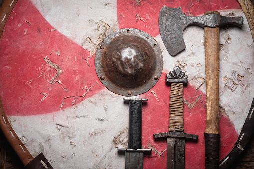 Old battle swords, axe and shield on the wooden table background top view.