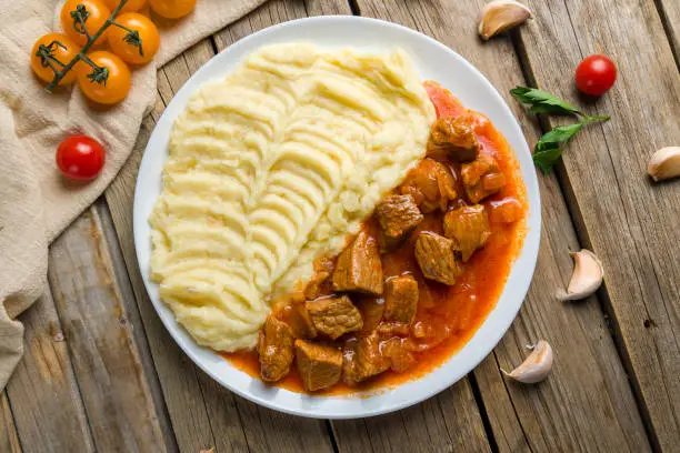 Photo of Goulash with beef and carrots with mashed potatoes top view on wooden table