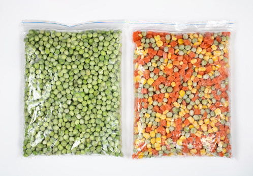 Mix of frozen vegetables in a package: carrots, corn grains, green peas on a white background, top view.