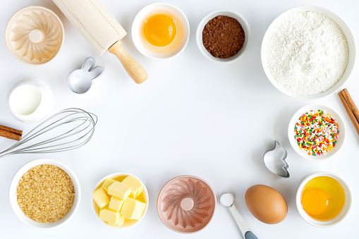 Baking ingredients frame: sugar, flour, eggs, cocoa, butter, cinnamon, baking powder, muffin tins, rolling pin, whisk. Ingredients for making dough, cakes, muffins, cookies.