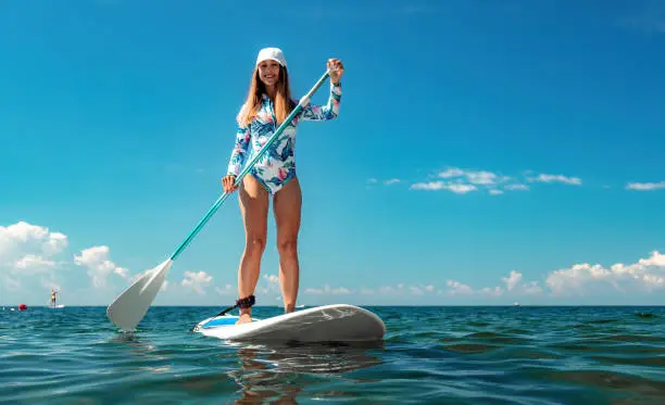 SUP Stand up paddle board. Young woman sailing on beautiful calm sea with crystal clear water. The concept of an summer holidays vacation travel, relax, active and healthy life in harmony with nature