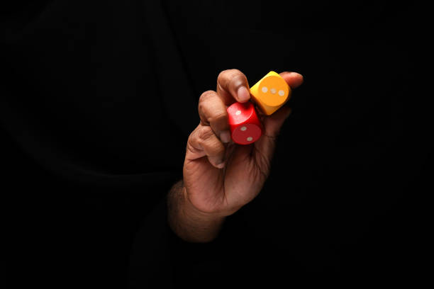 Asian male dark skinned single hand fist finger on black background holding wooden red yellow playing dice stock photo