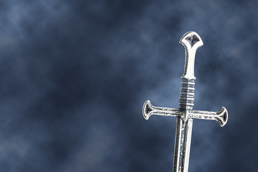 Mysterious and magical medieval sword / knightly arming sword, silver straight blade, double-edged weapon, single-handed, cruciform (cross-shaped) hilt. Gothic black background with scattering smoke