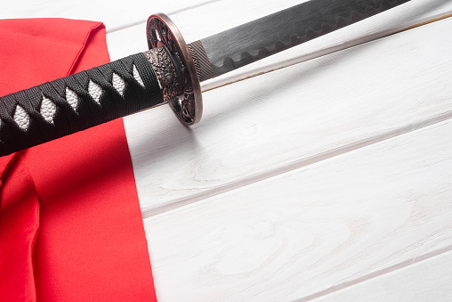 Katana sword and red waist band on the white table close up background.
