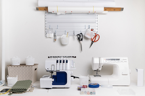 Workplace: White table with a sewing machine and an overlock for sewing. Large bright white room.