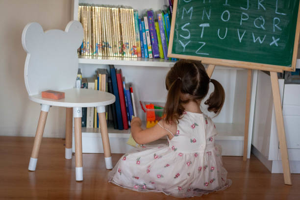 la niña está sentada en el suelo y leyendo libros. - teaching blackboard preschool alphabetical order fotografías e imágenes de stock