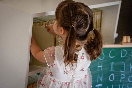 The young girl is standing on the chair, and putting back the book .