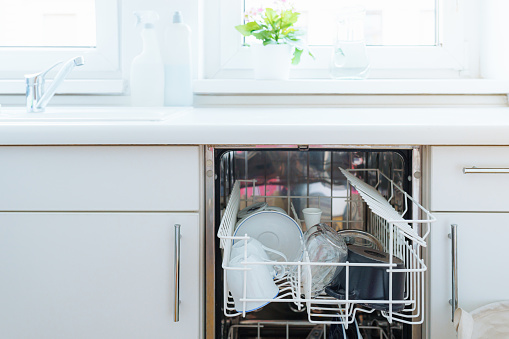 Built-in dishwasher with dirty dishes in the kitchen with white fronts. Dishwasher repair concept