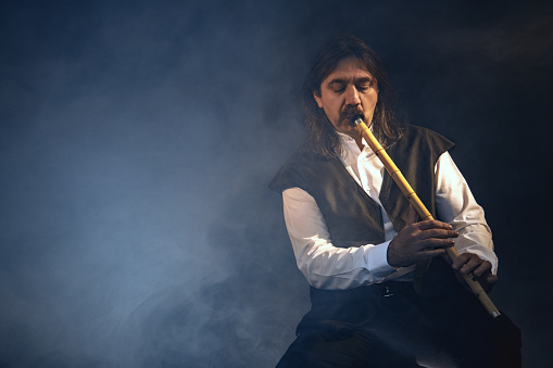 Turkish musician playing the reed flute  with black background and fogs