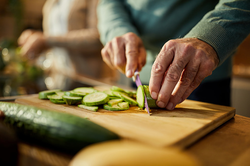 Close up of unrecognizable man cutting fresh zucchini for salad in the kitchen.