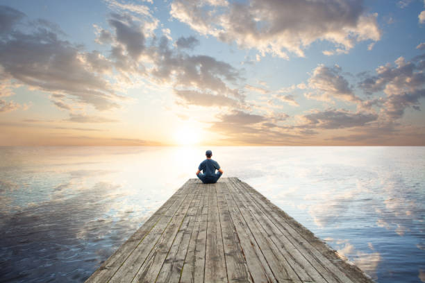 Man relaxing sitting on wooden jetty against sky clouds background