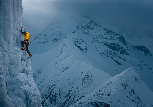 Strong man climbing a vertical ice wall in the mountains