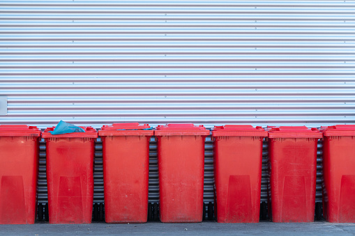 A row of red garbage cans in front of a corrugated iron wall