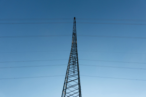 Close-up of a centrally positioned electricity pylon against a blue sky