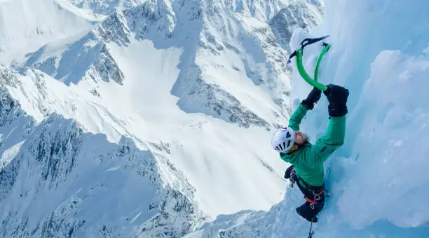 Strong mountaineer climbing ice on steep mountain face