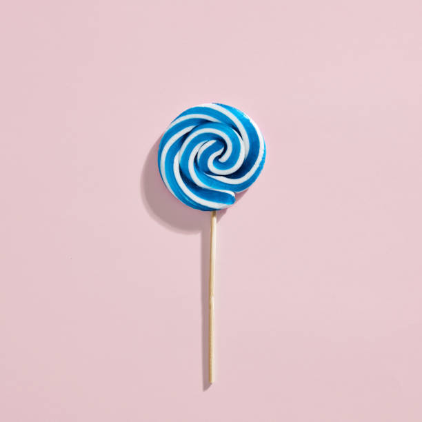 Blue and white colored swirl round candy lollipop on pink background.