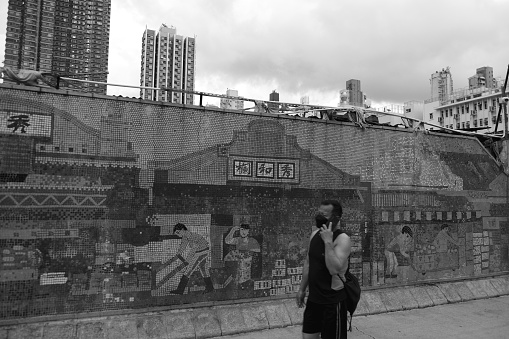 Man wearing protective face mask walking on a sidewalk by a graffiti wall of the historical Yau Ma Tei Wholesale Fruit Market in Kowloon. 
Hong Kong.