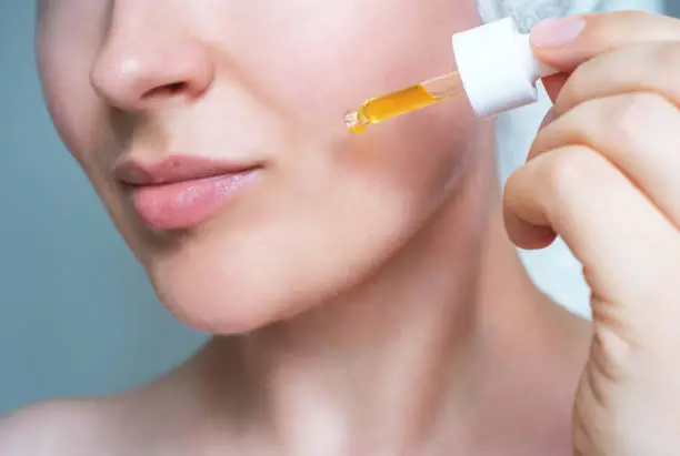 Female face and dropper with moisturizing serum close-up on a gray background.