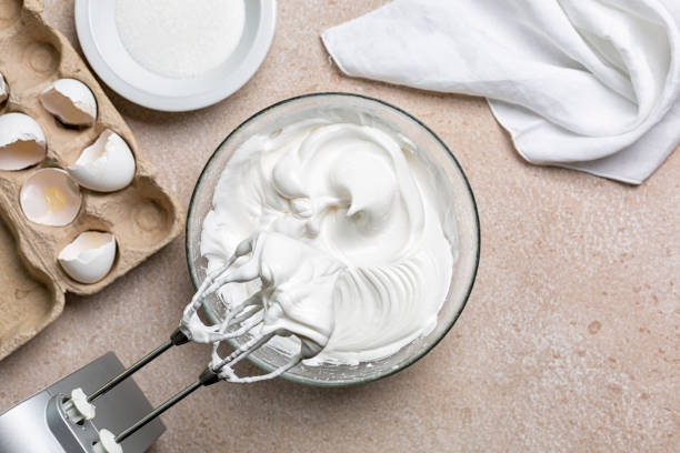 Beaten egg whites with sugar  for Meringue in a mixing bowl with an electric hand whisk. Cooking process with kitchen utensils. Beaten egg whites with sugar  for Meringue in a mixing bowl with an electric hand whisk. Cooking process with kitchen utensils. meringue stock pictures, royalty-free photos & images
