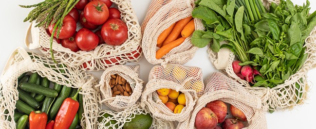 Top view of mesh eco reusable shopping bag with organic vegetables, fruits and groceries on white background.