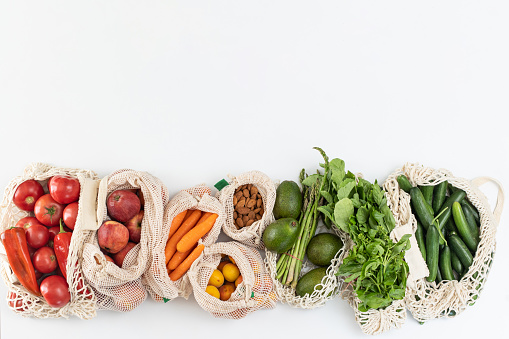 Top view of mesh eco reusable shopping bag with organic vegetables, fruits and groceries on white background.