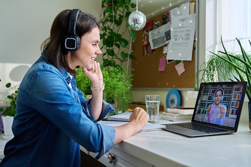 Female teacher in headphones teaching young student girl online. Sitting at home, high school teen pupil at laptop screen, talking female using video call chat conference. E-learning, remote lesson