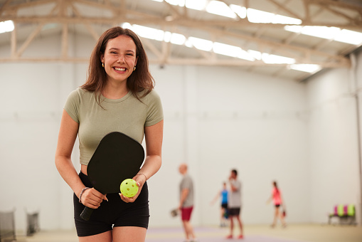 A portrait of a teenage girl holding a pickleball racquet and looking at the camera.